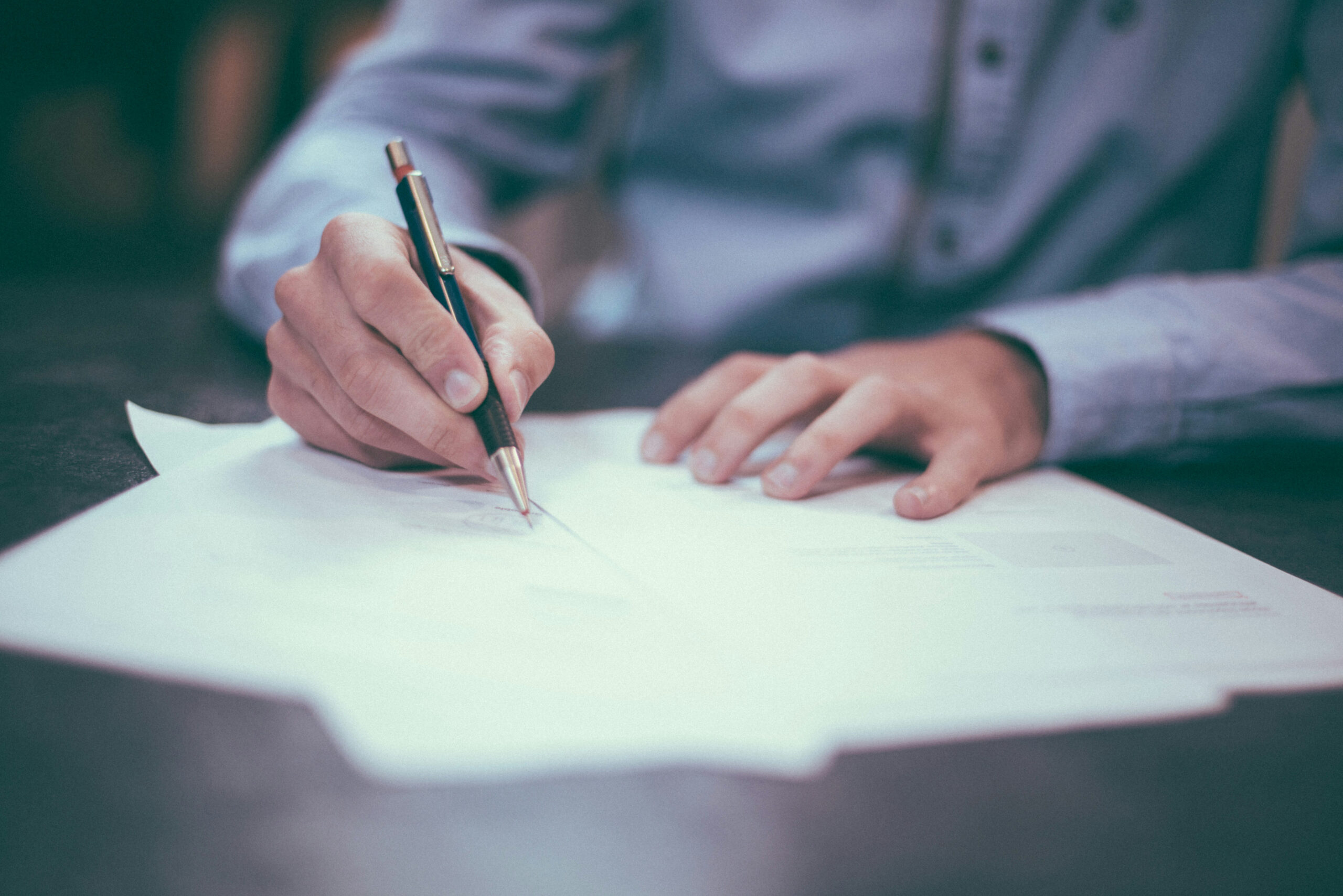 Person signing documents with a pen on papers placed on a table Person signing documents with a pen on papers placed on a table