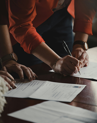 Person signing documents with a pen on papers placed on a table