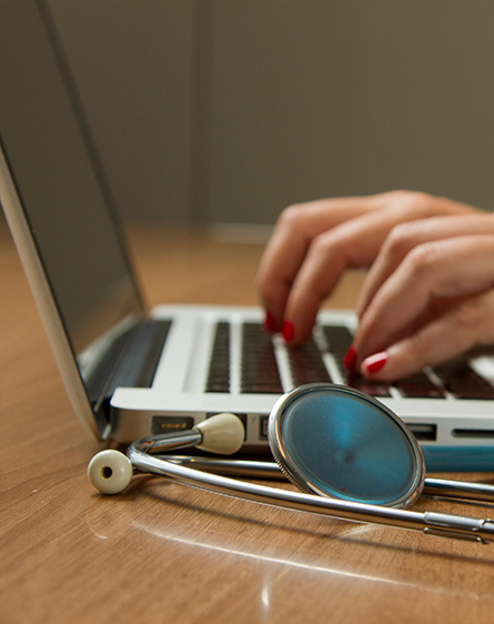 Hands typing on a laptop with a doctor's stethoscope beside it